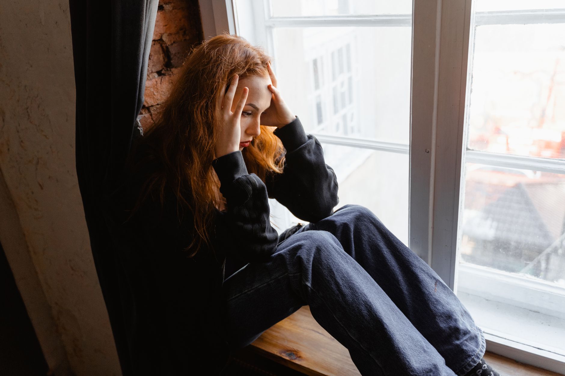 A young woman sitting by a window with her head in her hands
