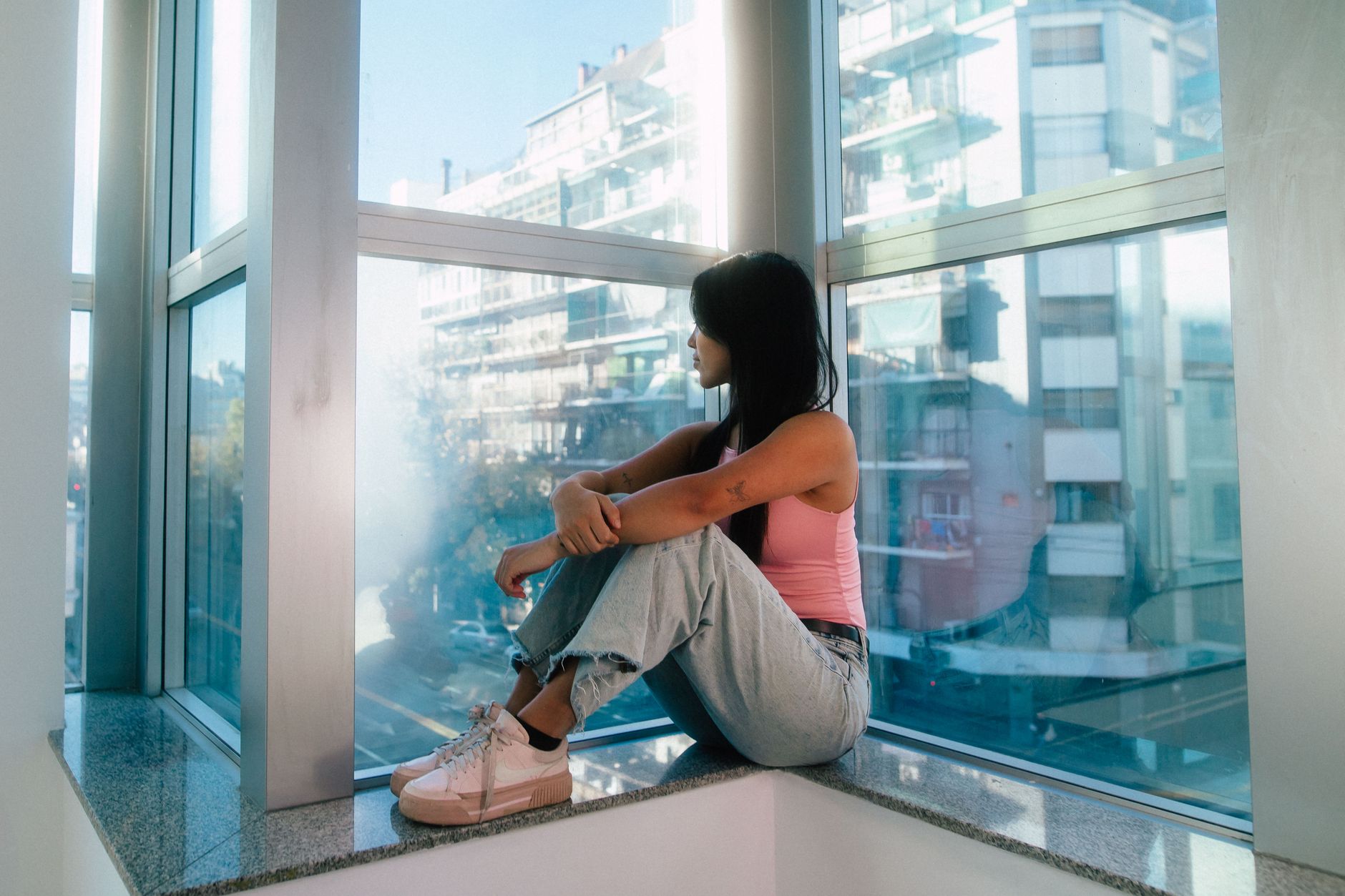 A woman sitting alone by a tall window, looking out